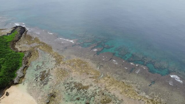 4K The serene seascape of Okinawa showcases crystal-clear waters, exposed rocky formations, and gentle waves lapping against the shore