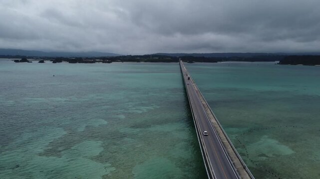 4K focus on road over Long bridge of Kouri Island and beach from a high view by drone with clear sky and sea water.