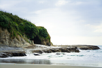 Sunset at Muriwai beach with waves splashing against the rocks and fishermen silhouettes in the...