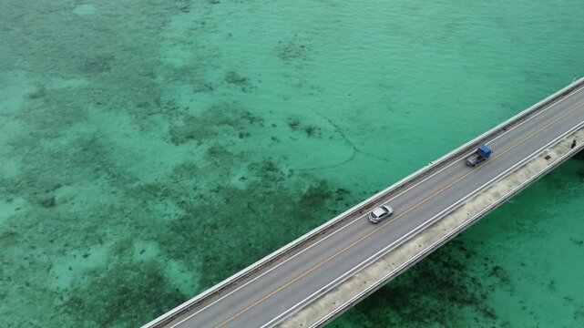 4K focus on road over Long bridge of Kouri Island and beach from a high view by drone with clear sky and sea water.