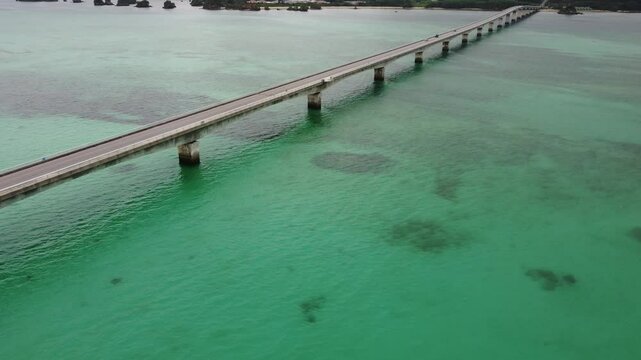 4K focus on road over Long bridge of Kouri Island and beach from a high view by drone with clear sky and sea water.