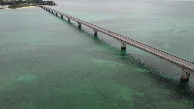 4K focus on road over Long bridge of Kouri Island and beach from a high view by drone with clear sky and sea water.