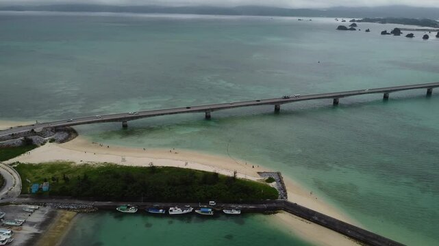 4K focus on road over Long bridge of Kouri Island and beach from a high view by drone with clear sky and sea water.