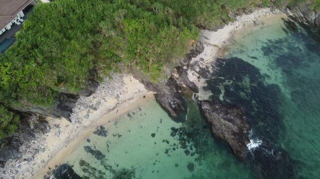4K over the serene seascape of Okinawa showcases crystal-clear waters, exposed rocky formations, and gentle waves lapping against the shore