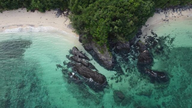 4K over the serene seascape of Okinawa showcases crystal-clear waters, exposed rocky formations, and gentle waves lapping against the shore