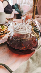 Glass teapot filled with herbal tea, marble table, restaurant setting.