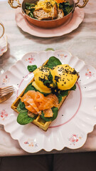 Eggs Benedict with smoked salmon served on a waffle with greens, plated elegantly.
