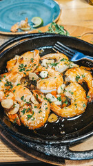 Sizzling shrimp dish with garlic and herbs on cast iron plate, served with fork.
