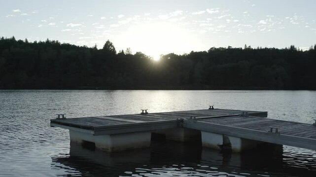 Aerial view flying over wooden boat dock on lake at sunset, sun reflecting on water, Marcillac La Croisille, France