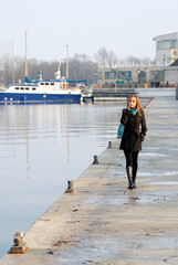 Young woman walking along a pier with boats docked nearby in a calm harbor..