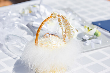 A close-up of a delicate wedding ring basket decorated with white feathers, satin ribbons, and...