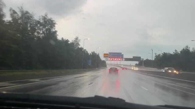 Car windscreen view driving Manchester orbital motorway M60 up onto the bridge in rain, fire brigade truck rushing past with blue emergency lights flashing.