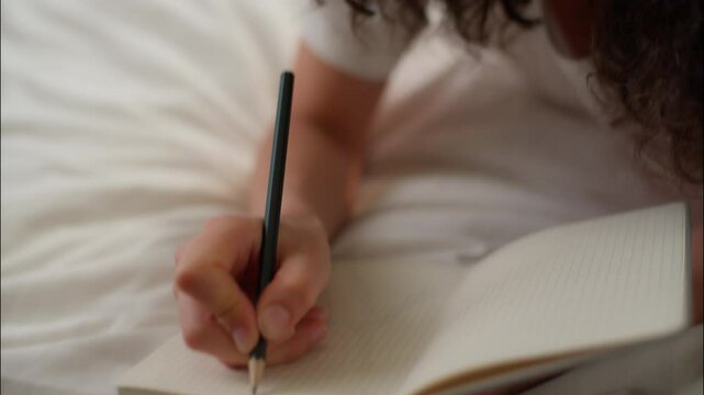 Writing notebook on bed Caucasian woman girl teen thoughtful write diary thoughts ideas planning tasks female student businesswoman in bedroom noting with pencil copybook notes studying home education