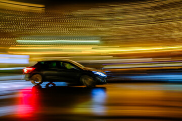 Motion blur captures a black vehicle speeding through a city street illuminated by festive lights...