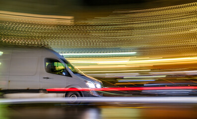 Motion blur captures a black vehicle speeding through a city street illuminated by festive lights...