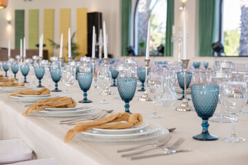 Formal banquet table ready for an event or wedding featuring layered white and glass dinner plates, silver cutlery, fancy cloth napkins and glassware with blue textured goblets for a vibrant contrast
