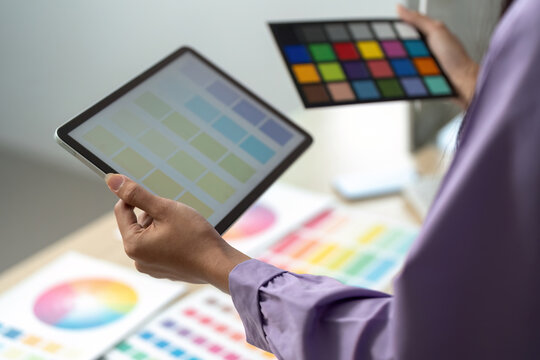 Graphic Design Tools. Designer comparing color swatches on tablet and printed palette.