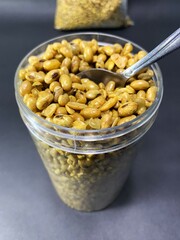 Delicious fried soybean snack. fried soybeans in a plastic jar with a spoon on dark background.