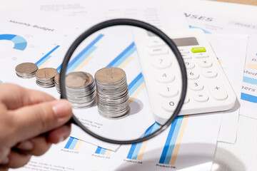 Magnifying Glass Over Coin Stacks on Graph – Representing Financial Review and Investment Focus