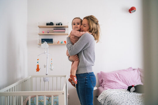 A loving mother holds her baby in a warm embrace in their home nursery. This tender moment captures the beautiful bond and love between mother and child.
