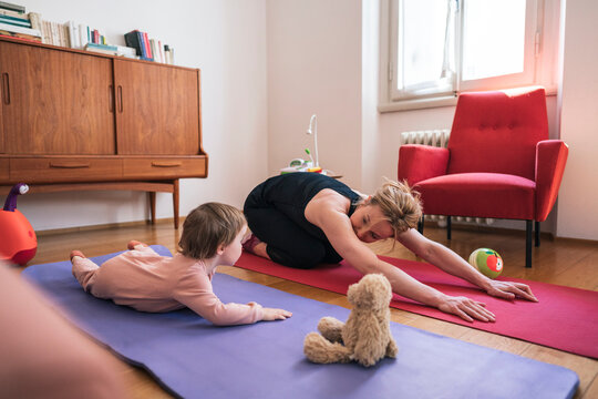 A mother and her young child enjoy a yoga session together at home. They are on colorful mats, stretching and spending quality time exercising indoors.
