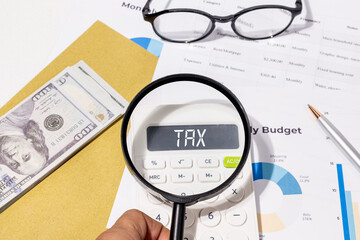 Tax Calculation Under Review &ndash; Magnifying Glass Focused on Calculator Display with Cash and Budget Chart