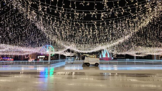 Zamboni resurfacing an ice rink under festive lights at night