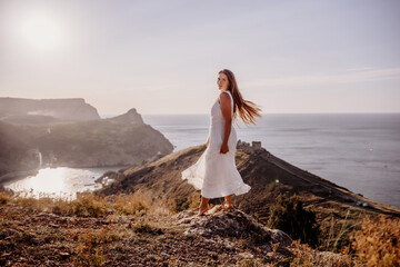 A woman in a white dress stands on a hill overlooking the ocean. The scene is serene and peaceful,...