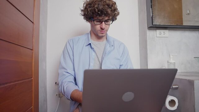 Caucasian man working urgently on his laptop while using the toilet, multitasking under pressure in a humorous and relatable everyday situation. work from home concept