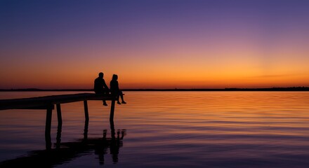 Fototapeta premium Silhouetted Couple Sitting on Wooden Pier Over Tranquil Lake at Sunset