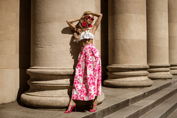 Elegant, stylish model in pink floral summer skirt and trendy ruffle top sensually walks around the...