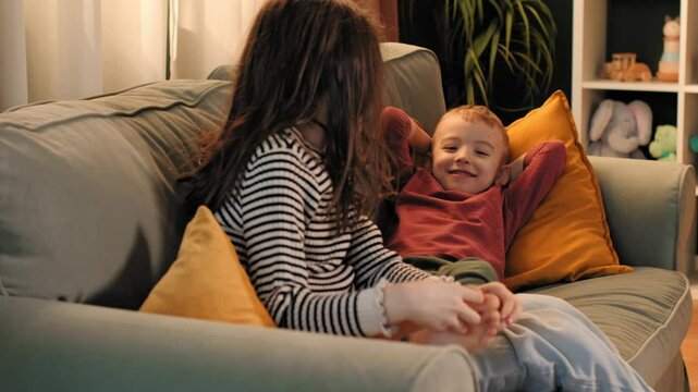 Sister tickling brother's feet on sofa, having fun at home