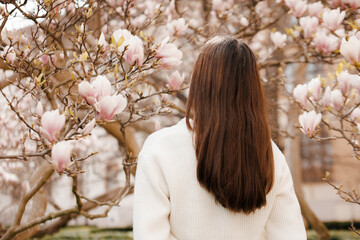 Young woman admiring blooming magnolia tree in springtime, turn back