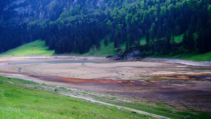 Dried lake bed surrounded by lush green mountains under a cloudy sky in early spring