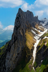 Dramatic mountain peak rises above green valleys and snowy slopes in bright daylight during summer season