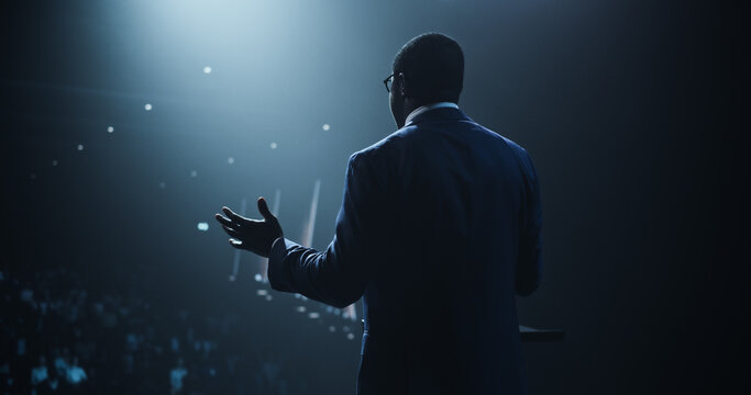 Business Leader Walking Out on Stage to Give a Talk at a Global Finance Summit. Audience Listening to His Insightful Talk. Speaker Standing with His Back to Camera While Making a Motivational Speech