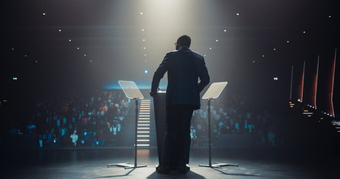 Anonymous Speaker Welcoming the Audience as He Goes on Conference Stage. Businessman Standing with His Back to Camera, Wearing a Suit, Speaking About Marketing at an International Business Meeting