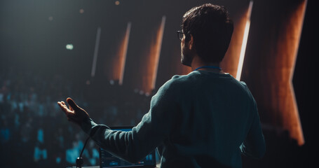Indian Entrepreneur in Glasses Shares an Insightful Talk on Technology and Leadership at a Professional Business Conference. Diverse Multiethnic Guests Sitting in a Dark Auditorium