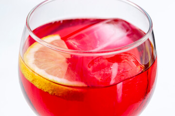 Close-up view of red aperitif drink with ice and lemon in a glass on white background