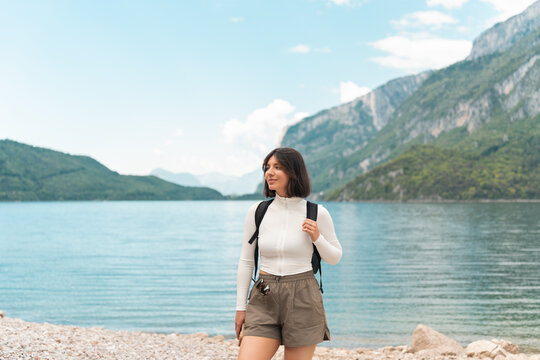 Lost in the moment, a happy woman hikes a quiet path between green hills, the lake glinting nearby and the mountains rising like a dream