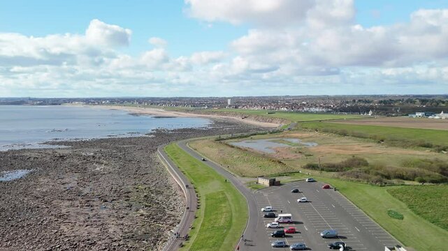 Whitley Bay UK: 13th April 2025. Access road and carpark to St Mary's Lighthouse. Drone shot of coastal area Cullercoats and Tynemouth on the horizon