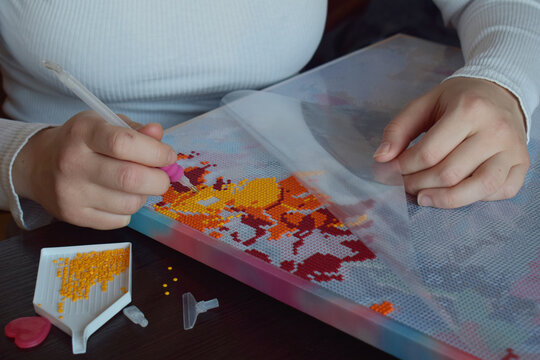 Woman creating a diamond painting by placing tiny colorful beads on a canvas perfect for DIY hobbies creative projects handmade artwork and artistic craft tutorials