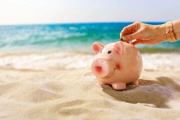 Piggy bank on soft golden sand under a clear blue sky on a hot summer day. Sunny beach sand with...