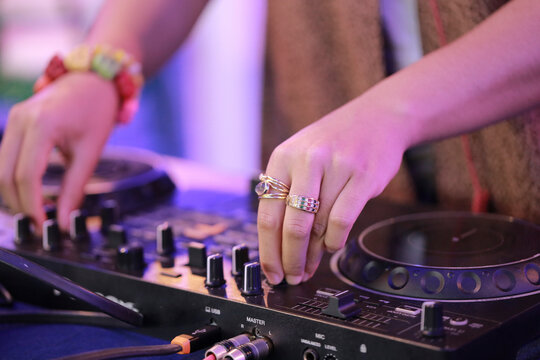 A detailed close-up shot of a female DJ's hand operating a turntable, capturing the essence of a live DJ performance. The image highlights the turntable's jog wheel, knobs, and faders, 