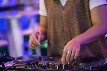 A detailed close-up shot of a female DJ's hand operating a turntable, capturing the essence of a live DJ performance. The image highlights the turntable's jog wheel, knobs, and faders, 