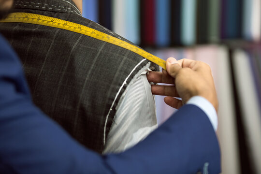 Close-up of bespoke tailor taking measurements of client for a suit with yellow measurements tape