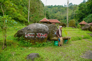 Asian Muslim woman sitting near a large stone with Indonesian writing that means soulmate stone...