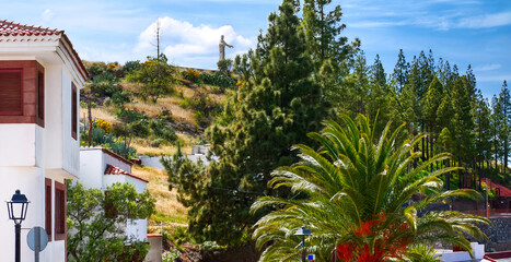 Village street in Artenara with palms, pines, and view of the sacred rock with Christ statue on the hill Gran Canaria, Spain