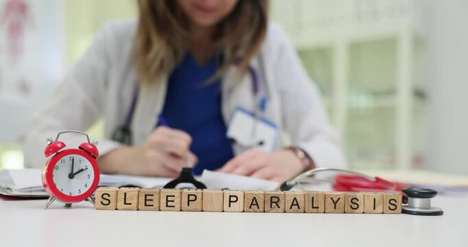 Inscription Sleep Paralysis of wooden cubes and alarm clock on doctor desk. Female physician chooses treatment from body and mind disorder in clinic