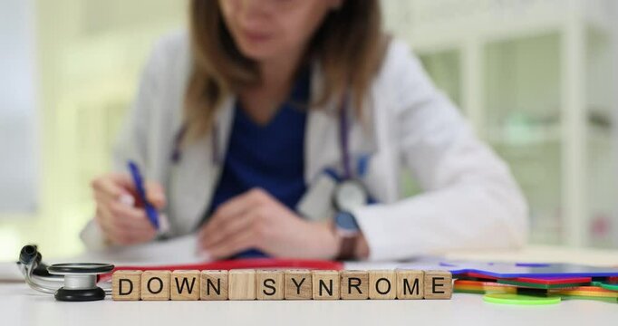 Phrase Down Syndrome on wooden cubes and working doctor in hospital. Woman medic documents diagnosis of genetic disorder at appointment slow motion
